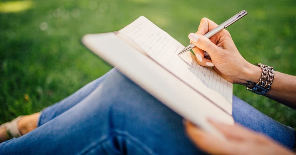 woman sitting on the grass writing a letter