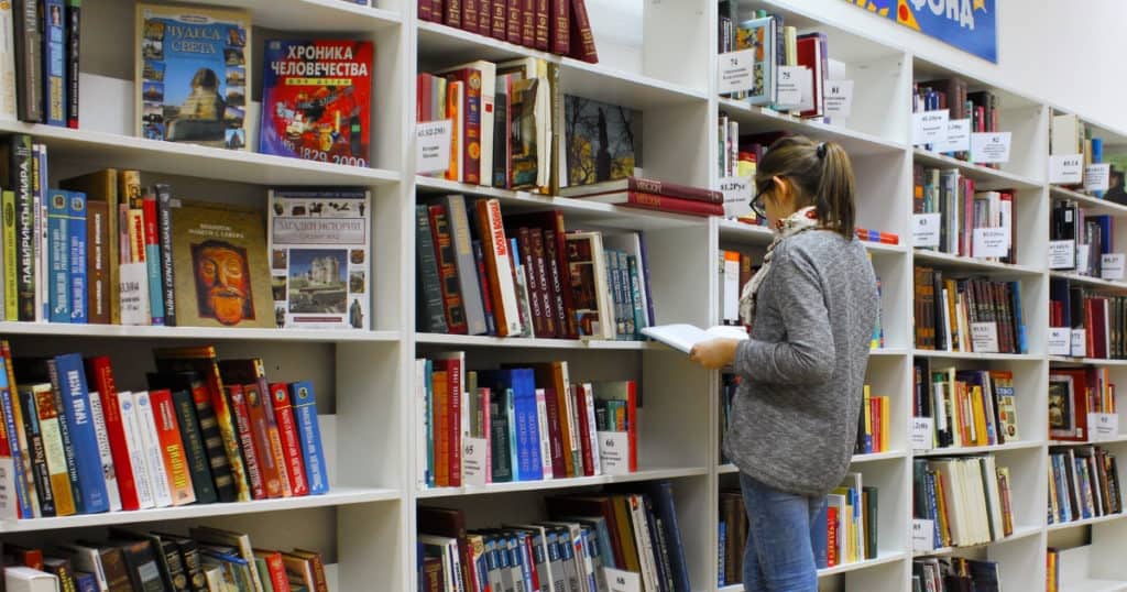 girl standing in college library looking at books