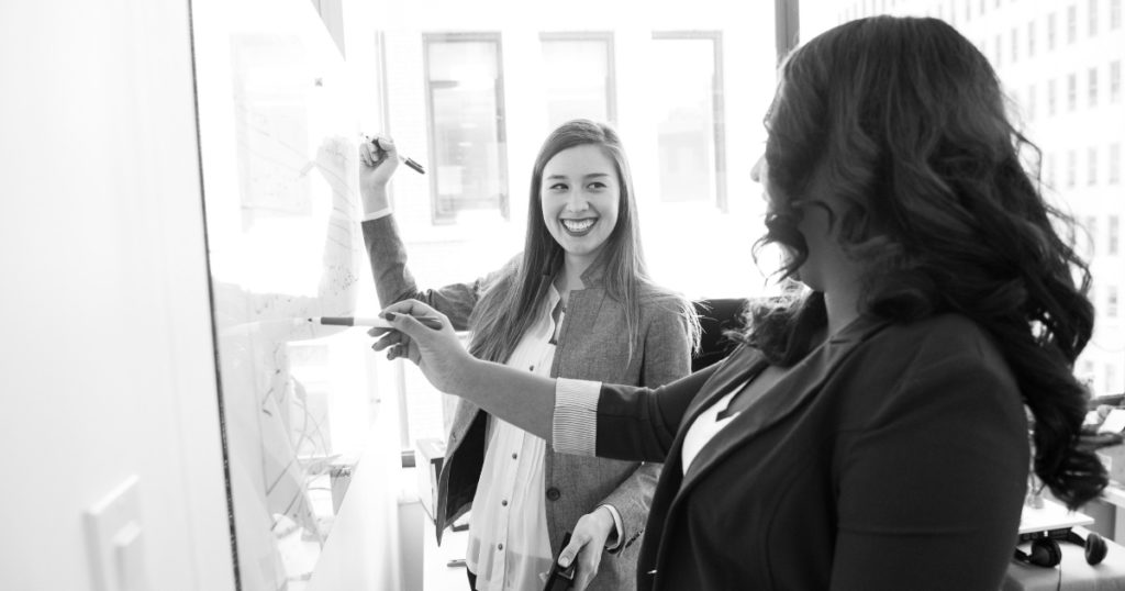 two woman working together on a white board while in college