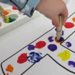 child using clothes pin to paint with a pom pom for crafts with kids