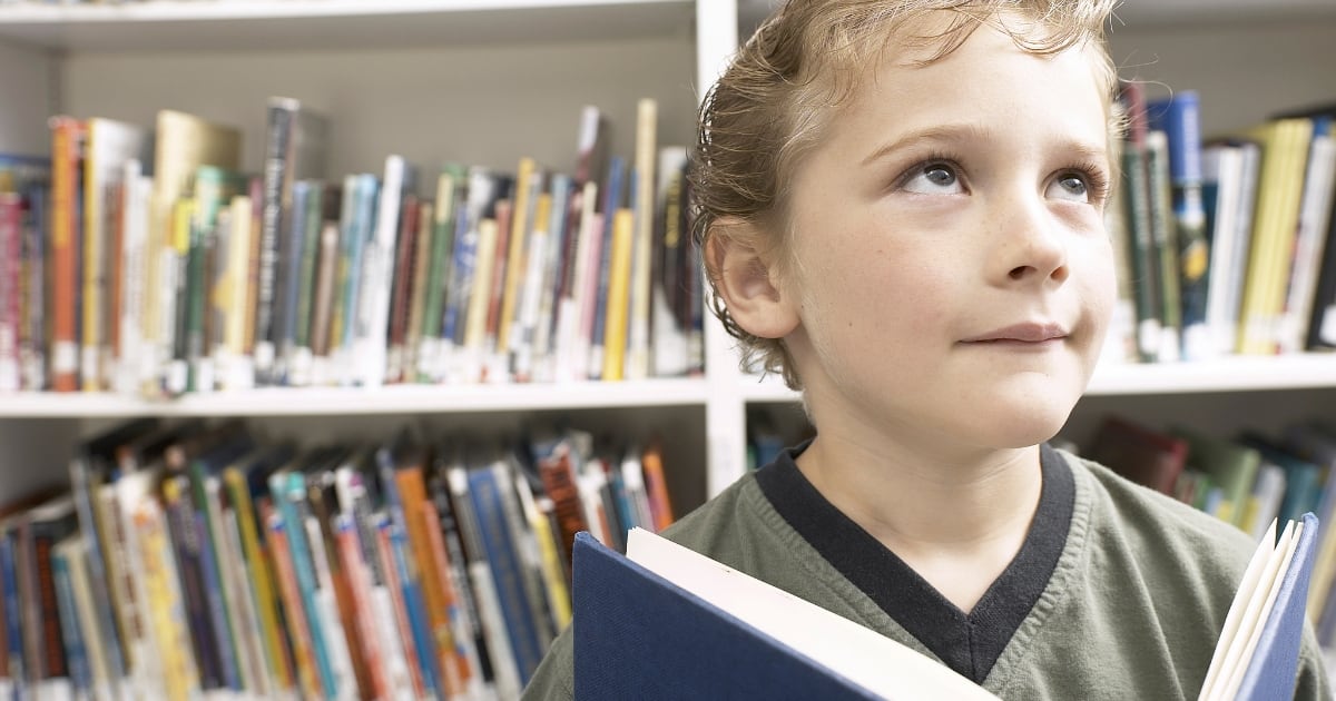 Blonde young boy with an open book in front of library shelves