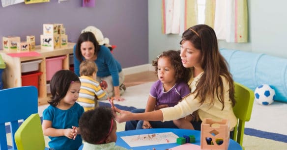 children in daycare setting coloring at a table with teacher