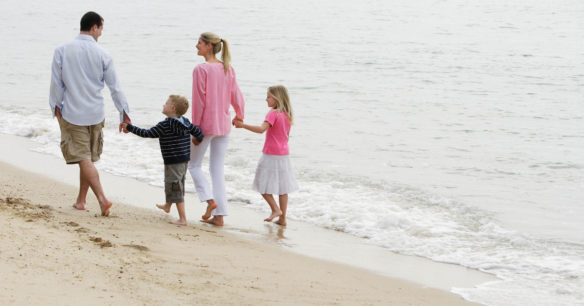 a family who has it all walking together hand in hand on the beach / mom, dad, little boy and little girl